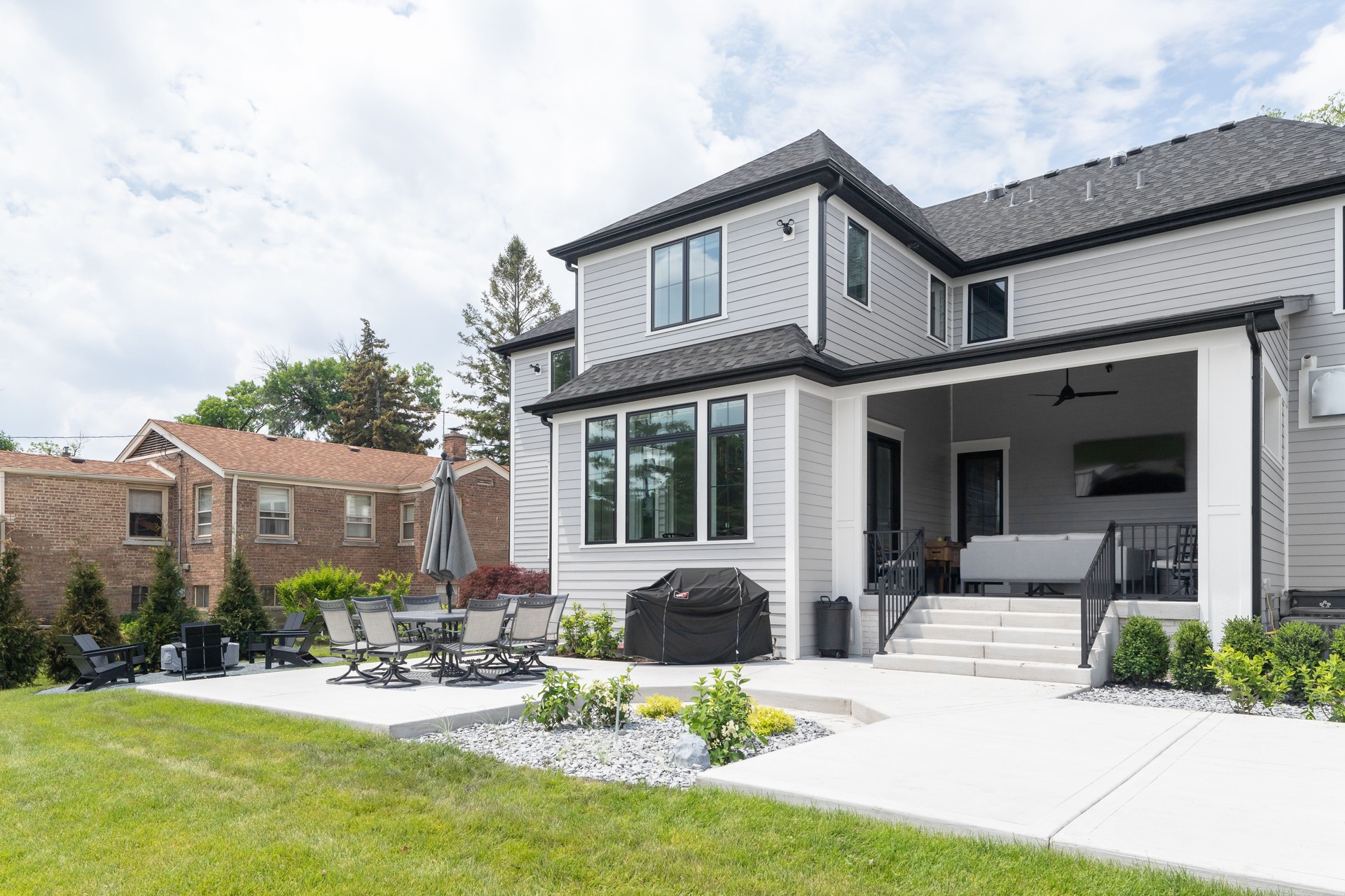 The backyard of a beautiful, grey home with a concrete patio.